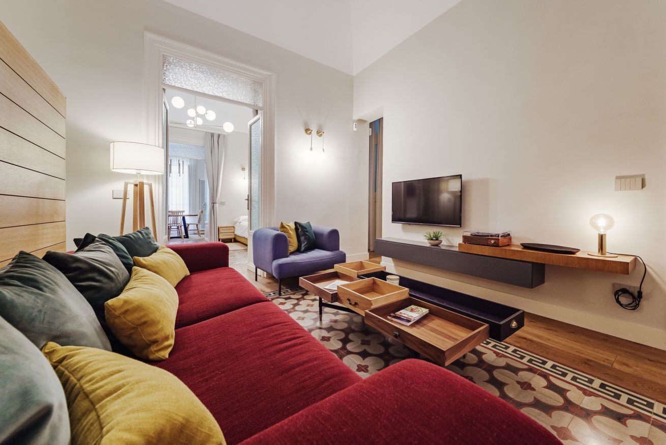 A modern living room with a red sofa, a blue armchair, a TV, and a wooden coffee table.