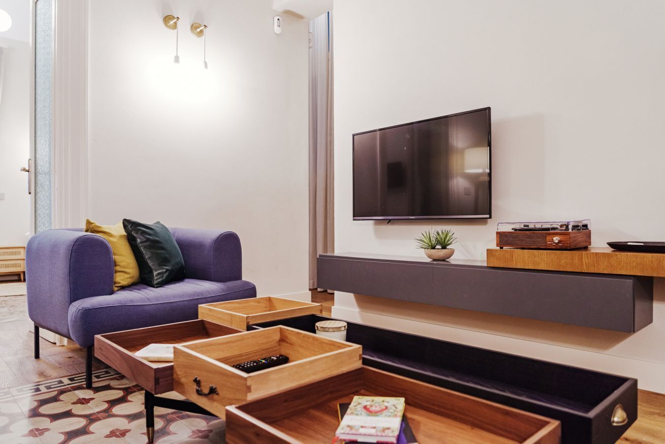 A modern living room with a sofa, wooden storage units, a flat-screen TV, and a small plant on a shelf.