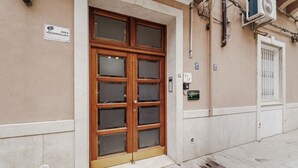 Une entrée d’immeuble avec une porte en bois, un panneau indiquant une zone sous vidéosurveillance et un appareil de climatisation fixé au mur.