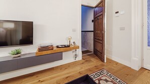 Un salon moderne avec un téléviseur à écran plat, une console en bois, une plante en pot et un tapis à motifs.