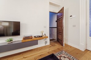 Ein modernes Wohnzimmer mit Flachbildfernseher, Holzkonsole, Blumentopf und einem gemusterten Teppich.