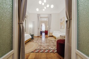 A hotel room with two beds, a patterned floor, a chandelier, and a view through a curtain. - Charming and modern 117 sq m apartment, accommodating up to 6 people, located on the first floor of a renovated building with an elevator. The property is strategically located, 700 meters from the historic Mercato del Capo and 500 meters from the Teatro (Palermo)