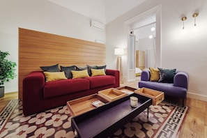A modern living room with a red sofa, a purple sofa, a wooden headboard, and a patterned rug. - Charming and modern 117 sq m apartment, accommodating up to 6 people, located on the first floor of a renovated building with an elevator. The property is strategically located, 700 meters from the historic Mercato del Capo and 500 meters from the Teatro (Palermo)