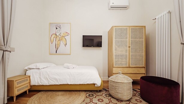 Une chambre à coucher comprenant un lit, une télévision, une armoire, un pouf en osier et un radiateur.