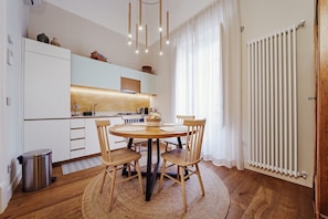 Eine moderne Küche mit weißen Schränken, einem runden Holztisch und einer Heizung.