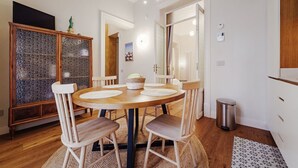 Un coin repas comprenant une table ronde, des chaises, un meuble avec une porte en verre et une poubelle.