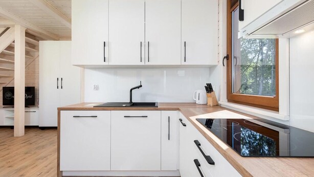 Une cuisine moderne avec des meubles blancs, un évier noir et une fenêtre donnant sur les arbres.