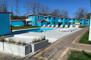 A swimming pool with lounge chairs, a children's play area, and a row of blue buildings. - Comfortable holiday home (No. 2), summer pool (Rewal)