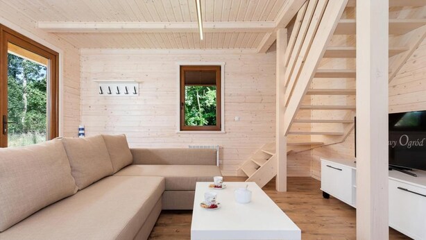 Et moderne interiør med trægulv, en beige modulsofa, et hvidt sofabord med kopper og tepotte, et fjernsyn på et hvidt skab, og en trætrap.