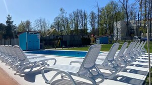 Un'area piscina con lettini bianchi disposti in file, un deposito di servizio blu e un cielo azzurro limpido.