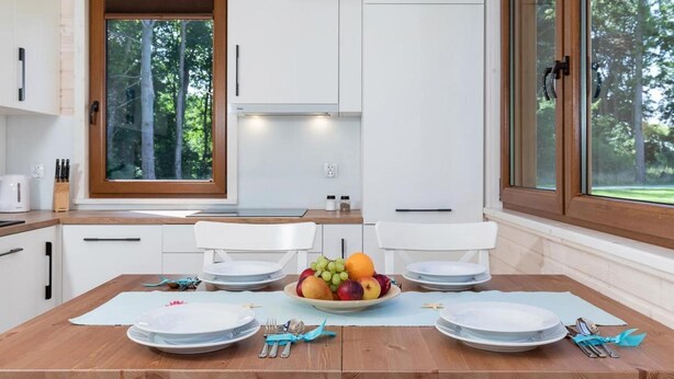 Una cucina moderna con mobili bianchi, un tavolo da pranzo in legno apparecchiato con piatti, posate e una ciotola di frutta.