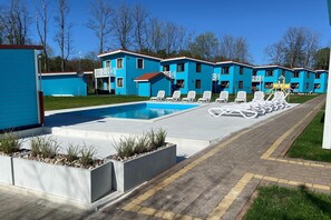 Ein Swimmingpool mit Liegestühlen, ein Spielbereich für Kinder und eine Reihe blauer Gebäude.