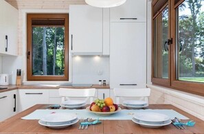 Une cuisine moderne avec des meubles blancs, une table à manger dressée pour quatre personnes et un panier de fruits posé sur la table.