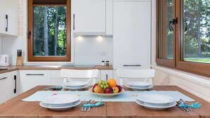 Una cocina moderna con armarios blancos, una mesa de comedor de madera dispuesta con platos, cubiertos y un tazón de fruta.