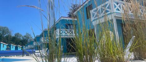 A building with a blue exterior and white architectural details, surrounded by tall grasses and a clear sky.
