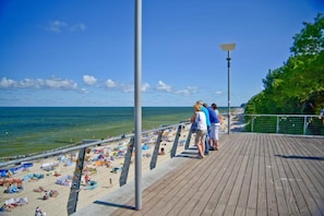 A wooden boardwalk with people walking, a beach with umbrellas and towels, and a clear blue sky. - Comfortable holiday home (no. 10), summer pool (Rewal)