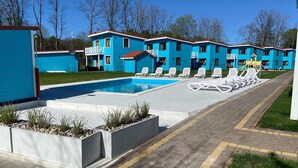A swimming pool with lounge chairs, a children's play area, and a row of blue buildings. - Comfortable holiday home (no. 10), summer pool (Rewal)