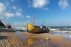 A beach with a yellow boat and a red boat on the sand. - Comfortable holiday home (no. 14), summer pool (Rewal)