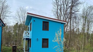 Una casa azul de dos pisos con un porche pequeño y un árbol en frente.