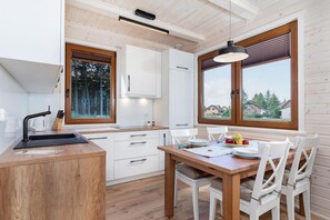 A modern kitchen with white cabinets, a wooden dining table, and two windows offering a view of the outside. - Comfortable holiday home (no. 14), summer pool (Rewal)