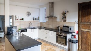 A modern kitchen with a central island, stainless steel appliances, and a wooden door. - Le grand gîte du domaine d'Embourg (Souvigny)