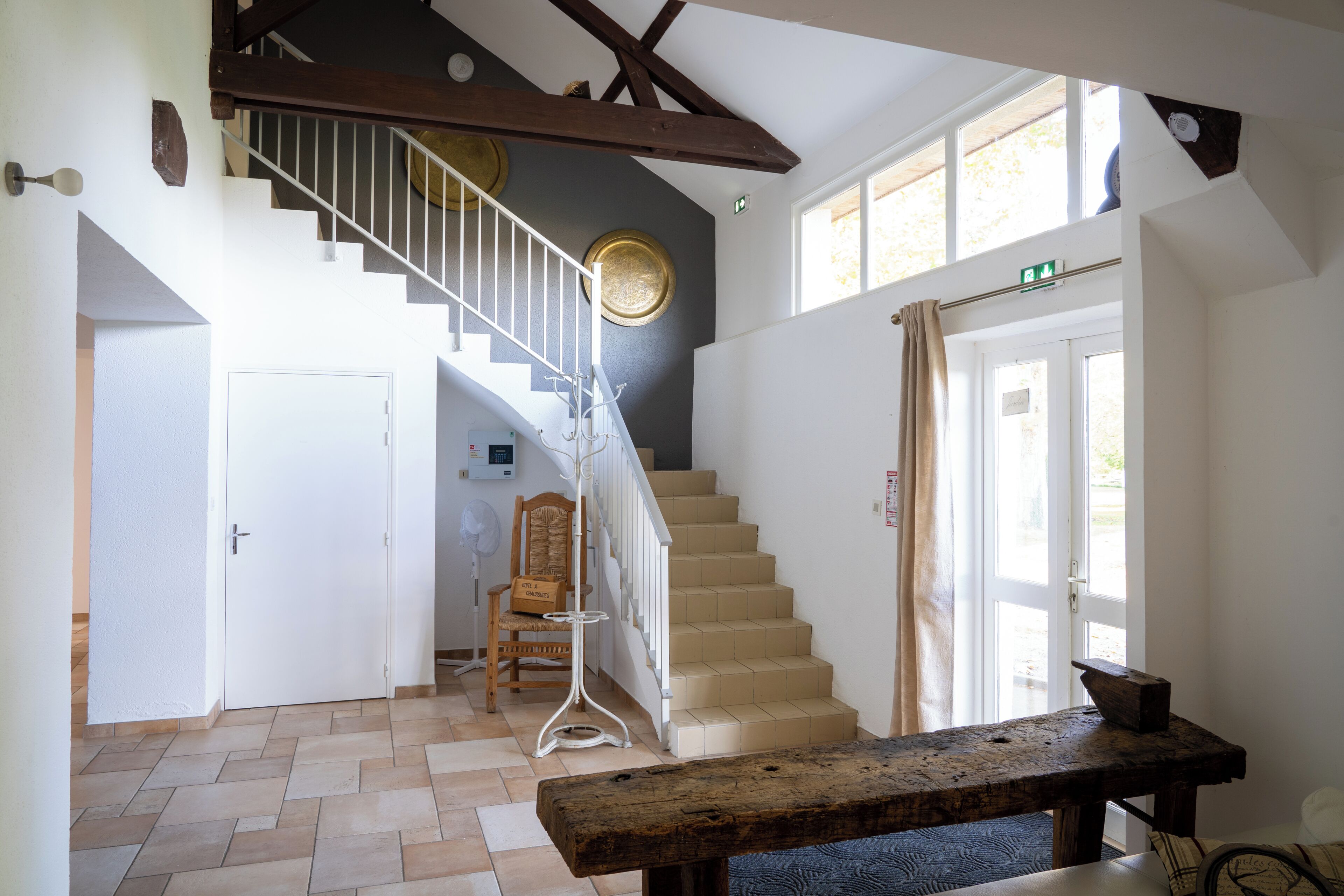 A staircase with a wooden handrail, a white door, and a bench in a room with tiled flooring and a ceiling fan.