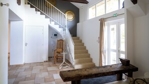 A staircase with a wooden handrail, a white door, and a bench in a room with tiled flooring and a ceiling fan. - Le grand gîte du domaine d'Embourg (Souvigny)