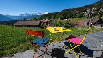 A table and two chairs on a stone patio with a mountain view.