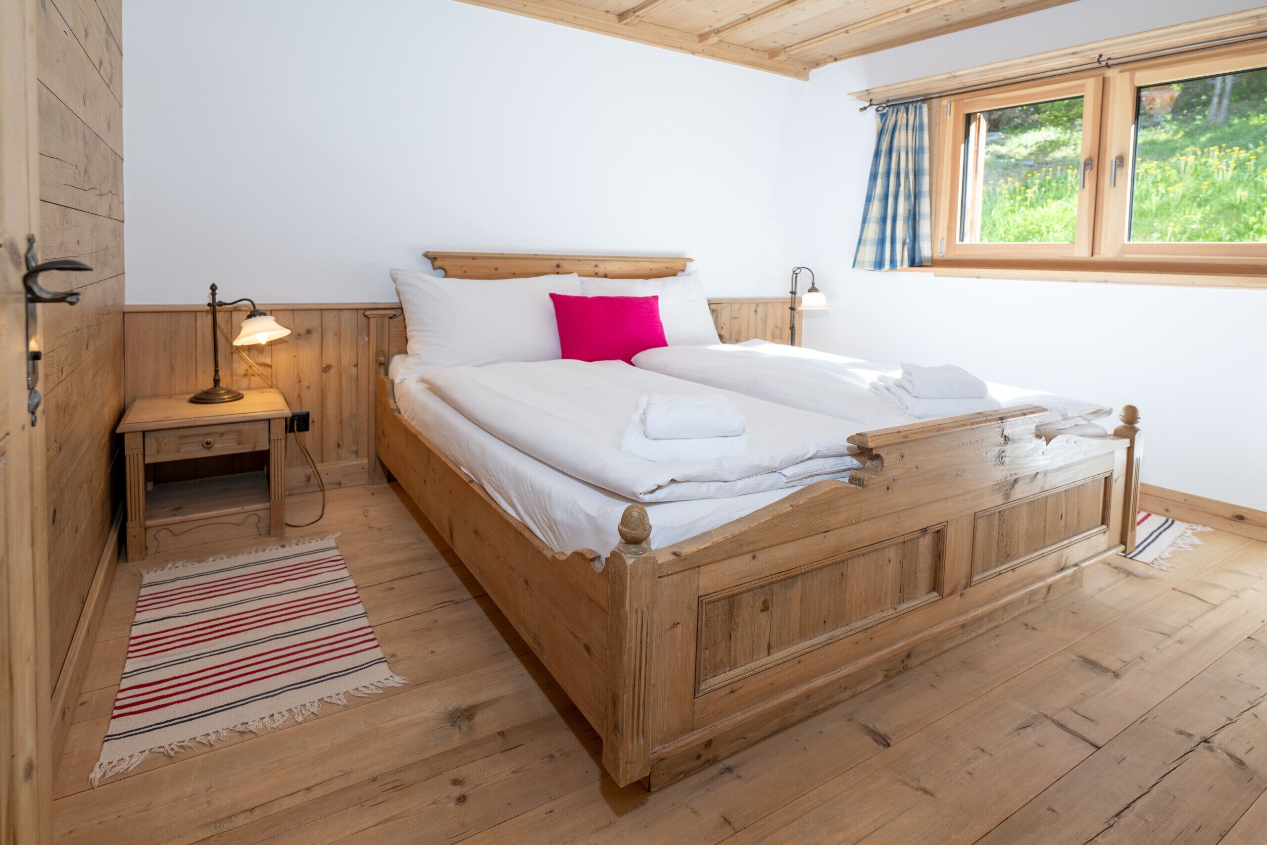 Una cama de madera con sábanas blancas, una mesita de noche con una lámpara y una ventana con cortinas.