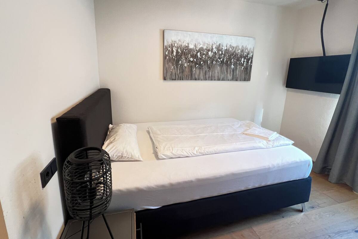 Ein Schlafzimmer mit einem Bett, einem an der Wand befestigten Fernseher und einem Deckenventilator.