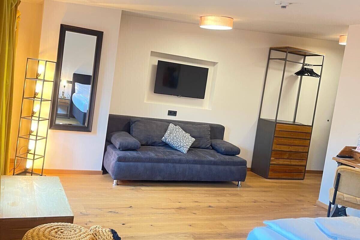Ein modernes Hotelzimmer mit einer Couch, einem an der Wand montierten Fernseher, Holzboden und einem Kleiderschrank.