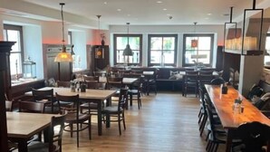 A spacious dining area with multiple tables and chairs, large windows, and a modern ceiling design.