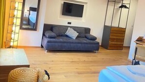 A modern hotel room with a sofa, a TV mounted on the wall, a wooden floor, a small table, and a bed.