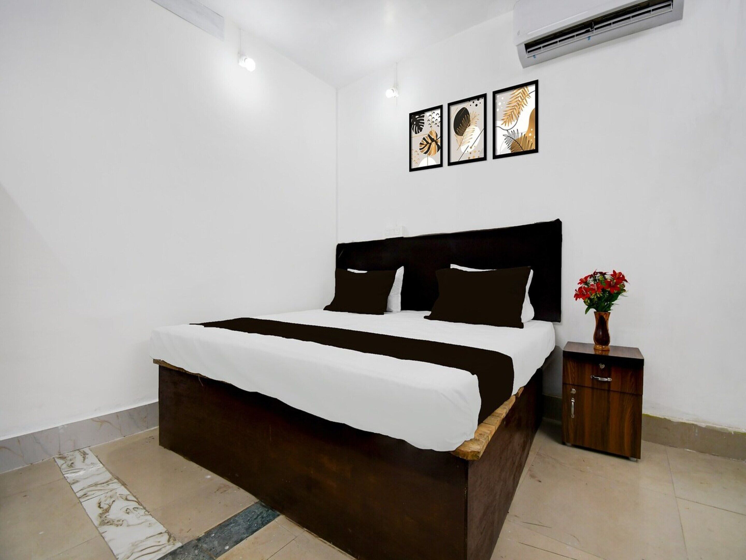 A bedroom with a bed, a nightstand, a vase with flowers, and three framed pictures on the wall.