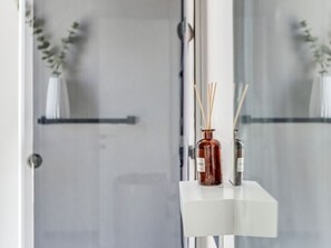 Divisória de chuveiro em vidro com prateleira branca que contém duas velas difusoras de fragrância.