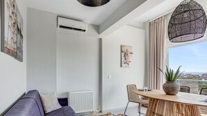 A modern living room with a purple sofa, a wooden dining table, and a large window with a view. - Verde Premium Apartments (Thessaloniki)