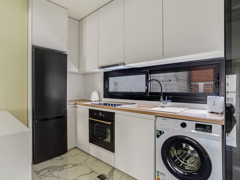 A compact kitchen with a refrigerator, oven, microwave, and washing machine.