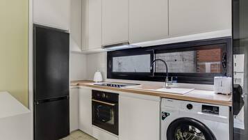 A compact kitchen with a refrigerator, oven, microwave, and washing machine.