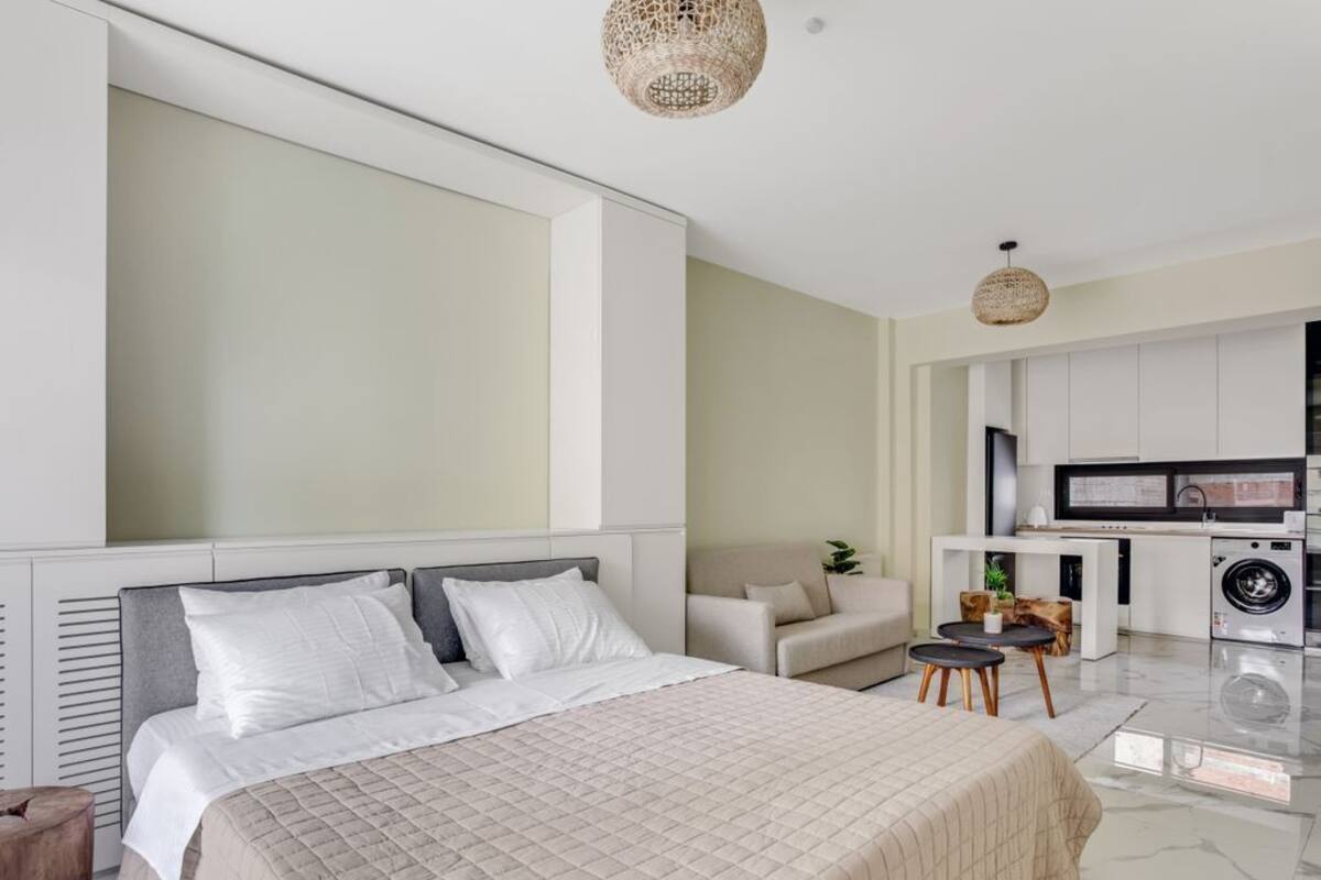 Une chambre moderne avec un grand lit, un canapé, une petite table et un lave-linge à l’arrière-plan.
