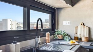 A modern kitchen with a large window, a black sink, a wooden cutting board, and a potted plant. - Verde Premium Apartments (Thessaloniki)
