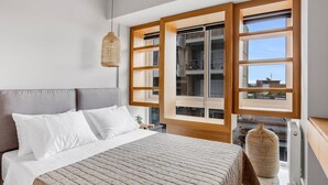 A bedroom with a large bed, a hanging light fixture, and a view of the city through large windows. - Verde Premium Apartments (Thessaloniki)