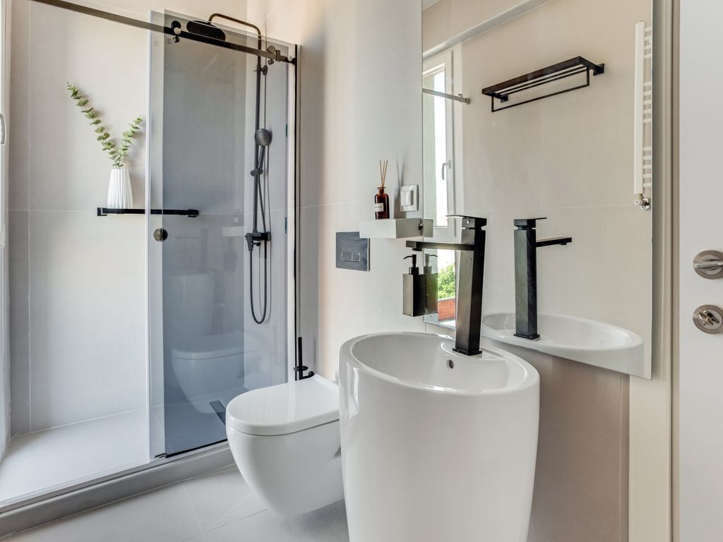 A modern bathroom with a glass-enclosed shower, a white toilet, and a large white sink with a mirror above it.