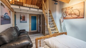 Un dormitorio tipo loft con escalera de madera, una cama, un sofá y un cuadro de bicicleta en la pared.