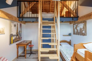 Een slaapkamer in loftstijl met een houten ladder, een stapelbed, bureau, stoel en kunstwerk.
