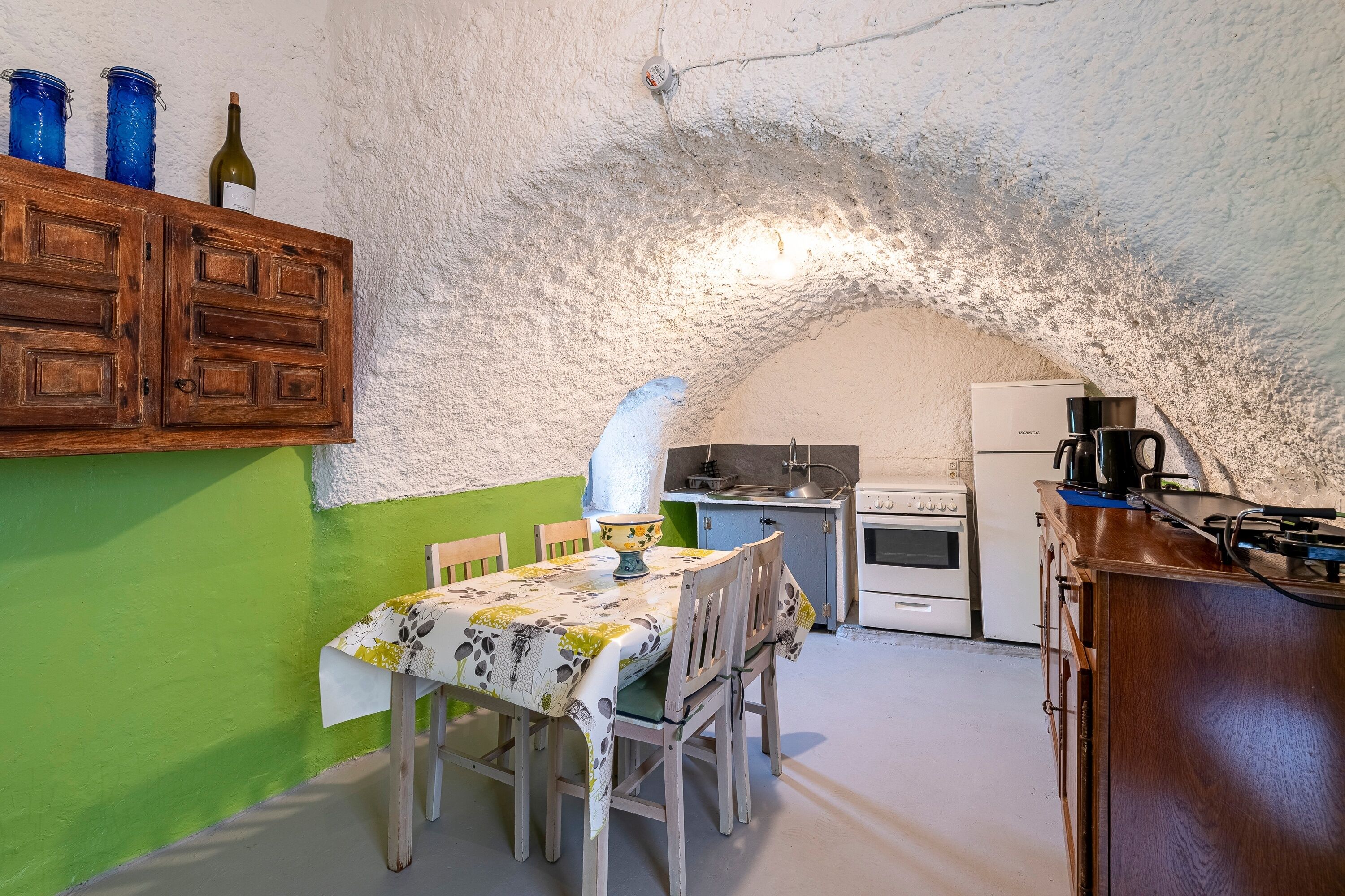 A rustic kitchen with a stone arch, wooden cabinets, a dining table with chairs, and a small kitchenette.