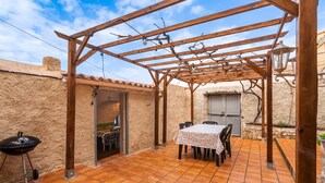 En overdækket terrasse med bord og stole, grill og pergola.