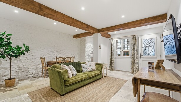 A cozy living room with a green sofa, wooden beams, a stone wall, and a dining area with a wooden table and chairs. - Robin's Nest – Cocon au cœur du Vieil Antibes (Antibes)
