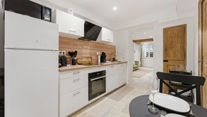 A modern kitchen with white cabinets, a built-in oven, and a dining area with a table set for two. - Robin's Nest – Cocon au cœur du Vieil Antibes (Antibes)