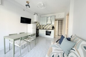 A modern kitchen with white cabinets, a built-in oven, and a dining area with a table and chairs.