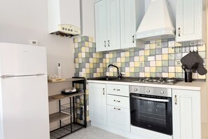 Une cuisine compacte avec des meubles blancs, une cuisinière à gaz, un four, un four à micro-ondes et un dosseret carrelé.